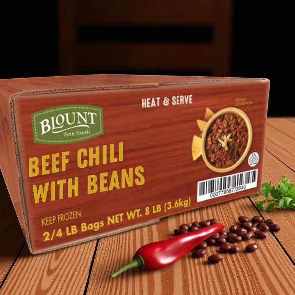 A box of Blount Fine Foods Frozen Beef Chili with Beans (2 packs, 4 lbs each) sits on a wooden table beside a red chili pepper and dried beans, ready to heat and serve for a hearty, savory meal.