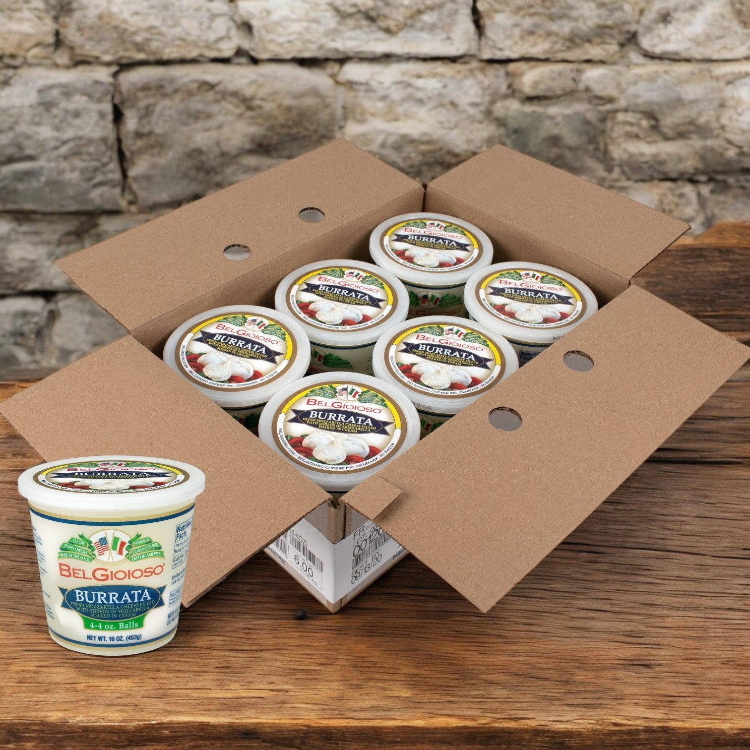 A cardboard box open against a stone wall reveals multiple containers of BelGioioso Fresh Mozzarella Burrata – 4 Ounce – 6/1 LB cheese. One container is outside the box, emphasizing the fresh mozzarella appeal of this Belgioioso delicacy.