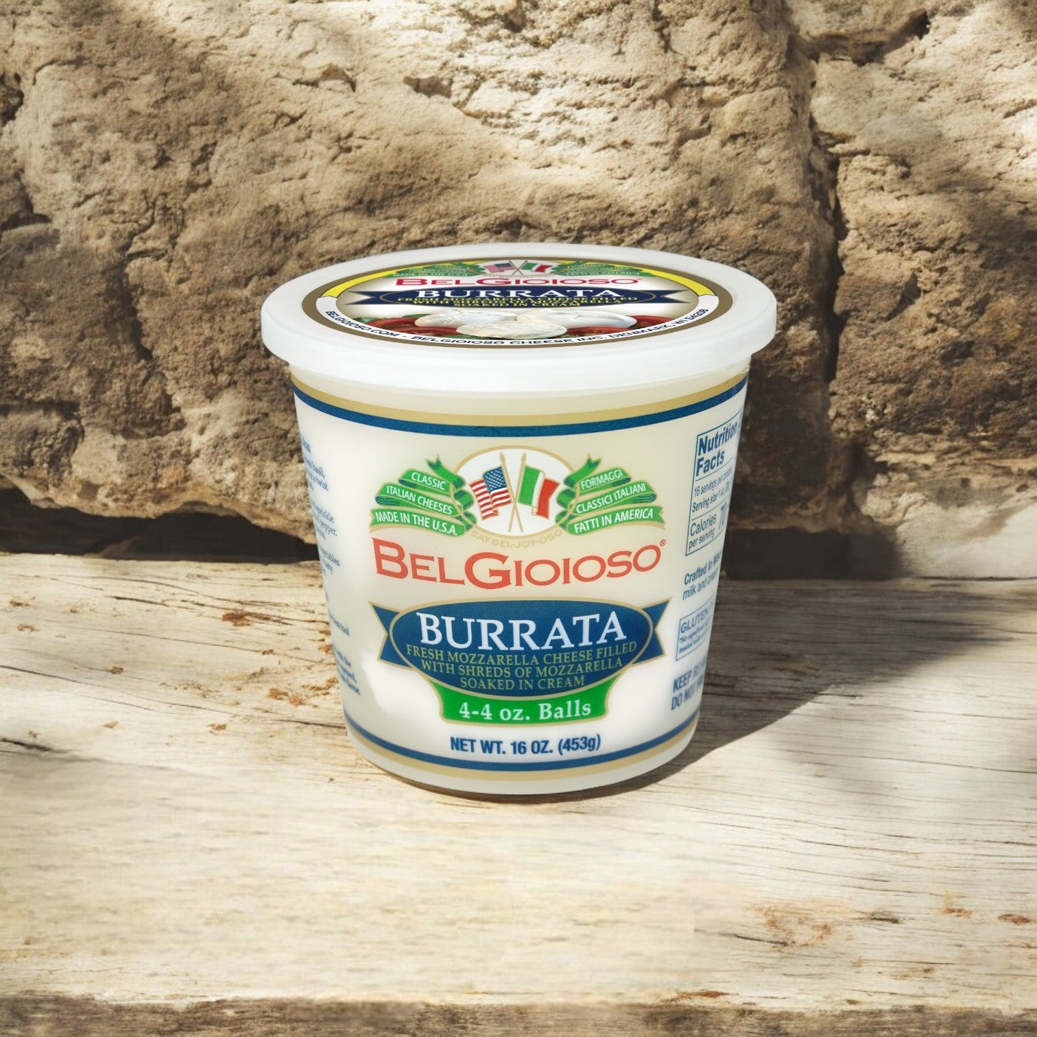 A container of BelGioioso Fresh Mozzarella Burrata – 4 Ounce – 6/1 LB, a luxurious cheese with a creamy core, sits elegantly on a wooden surface against a stone background.