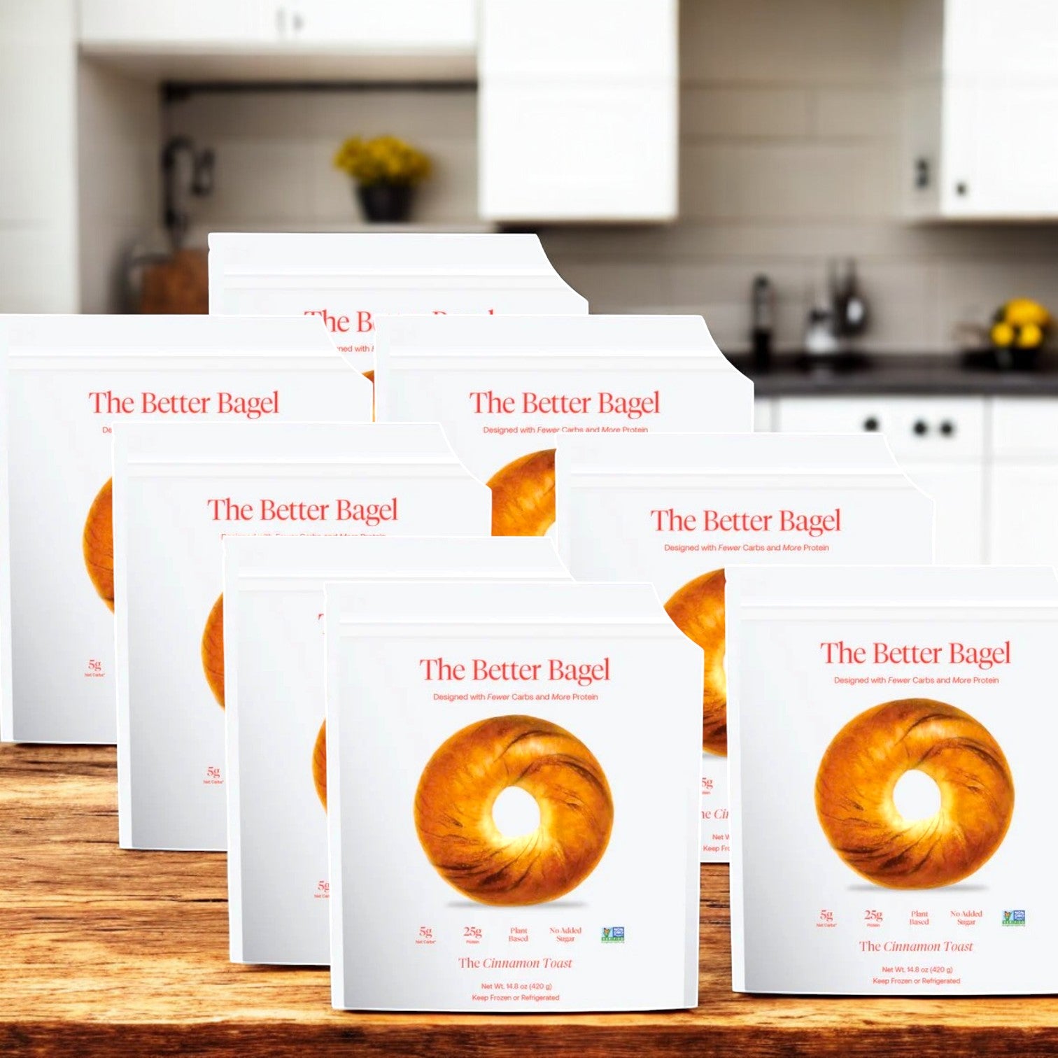 Eight bags of BetterBrand's "The Cinnamon Better Bagel" are arranged on a wooden surface in a cozy kitchen, showcasing their soft and chewy texture for an irresistibly delightful experience.