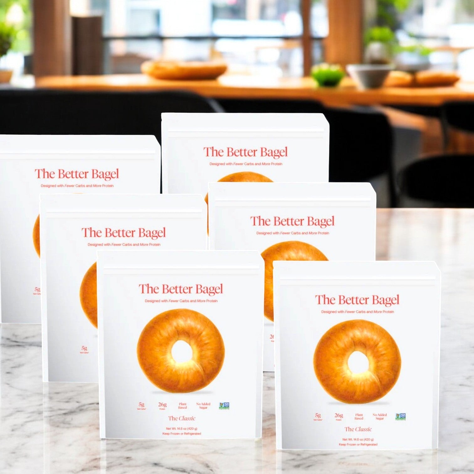 Boxes of "BetterBrand - The Classic Better Bagel" with high-protein alternative images are displayed on a marble counter. Each box contains 6 bags totaling 24 bagels.