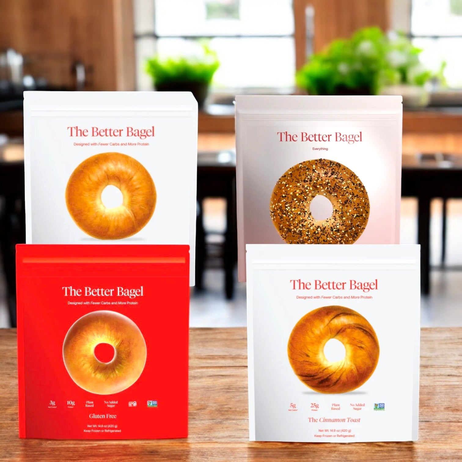 Four boxes of "BetterBrand Bagel Variety Pack – 32 Total Bagels!" are on the table, featuring flavors like Everything, Plain, Gluten-Free, and Cinnamon Toast. In the cozy kitchen background, a table and chairs add to the scene. In stock & ready to ship!.