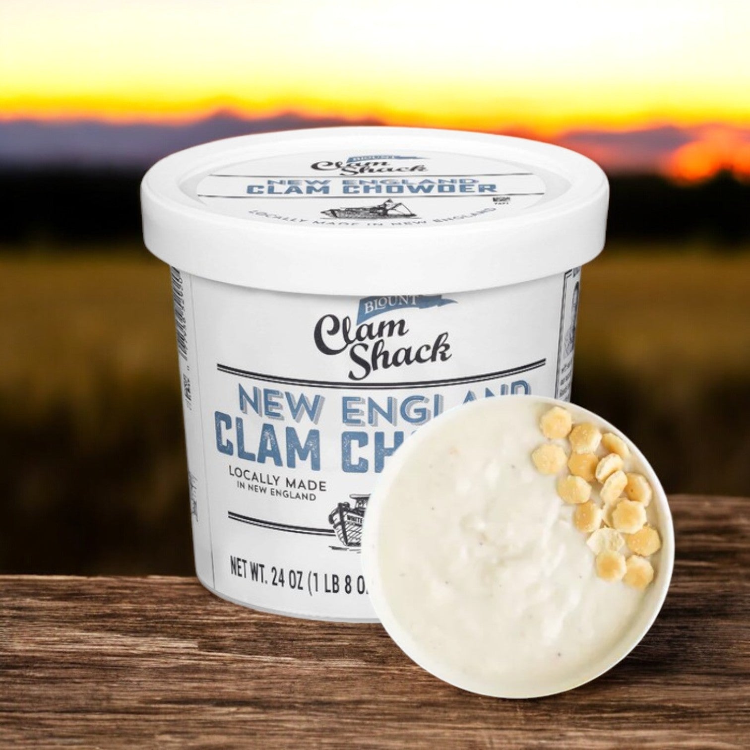 A container of Blount Fine Foods' Blount Clam Shack Gluten Free New England Clam Chowder Soup - 24 oz. sits beside a bowl with oyster crackers, as a sunset casts a warm glow over fields, setting the scene for this delightful soup crafted with premium ingredients.