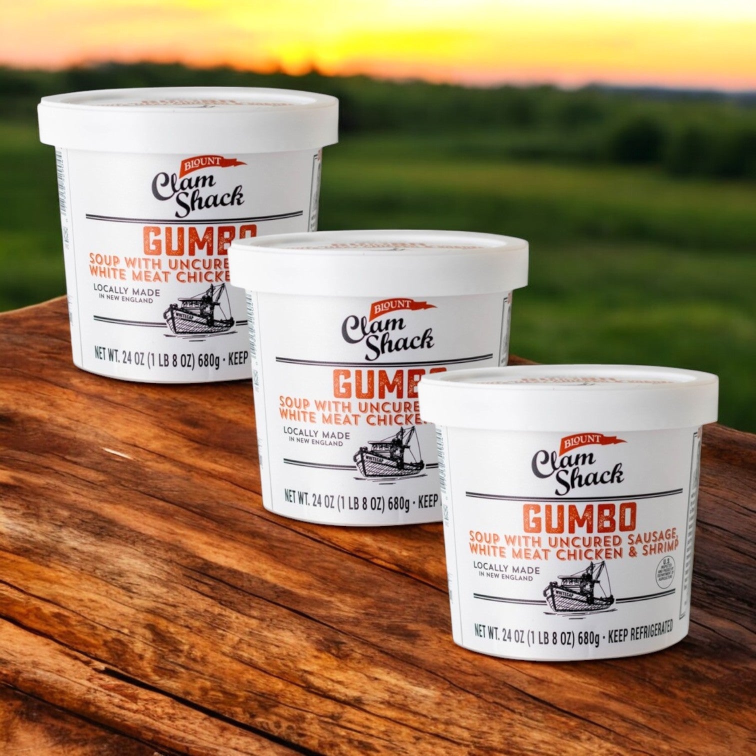Three tubs of Blount Fine Foods' Clam Shack Gumbo with Uncured Sausage, White Meat Chicken & Shrimp Soup, 3/24 oz., sit on a wooden surface against a blurred outdoor backdrop.