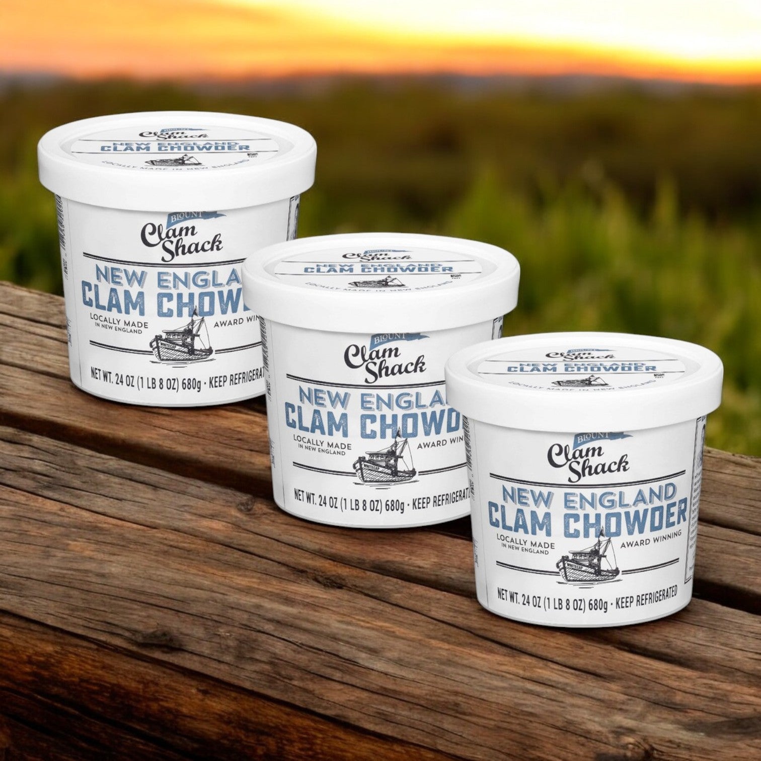 Three tubs of Blount Clam Shack Gluten Free New England Clam Chowder Soup by Blount Fine Foods, each 24 oz, are arranged on a wooden surface with a grassy background.