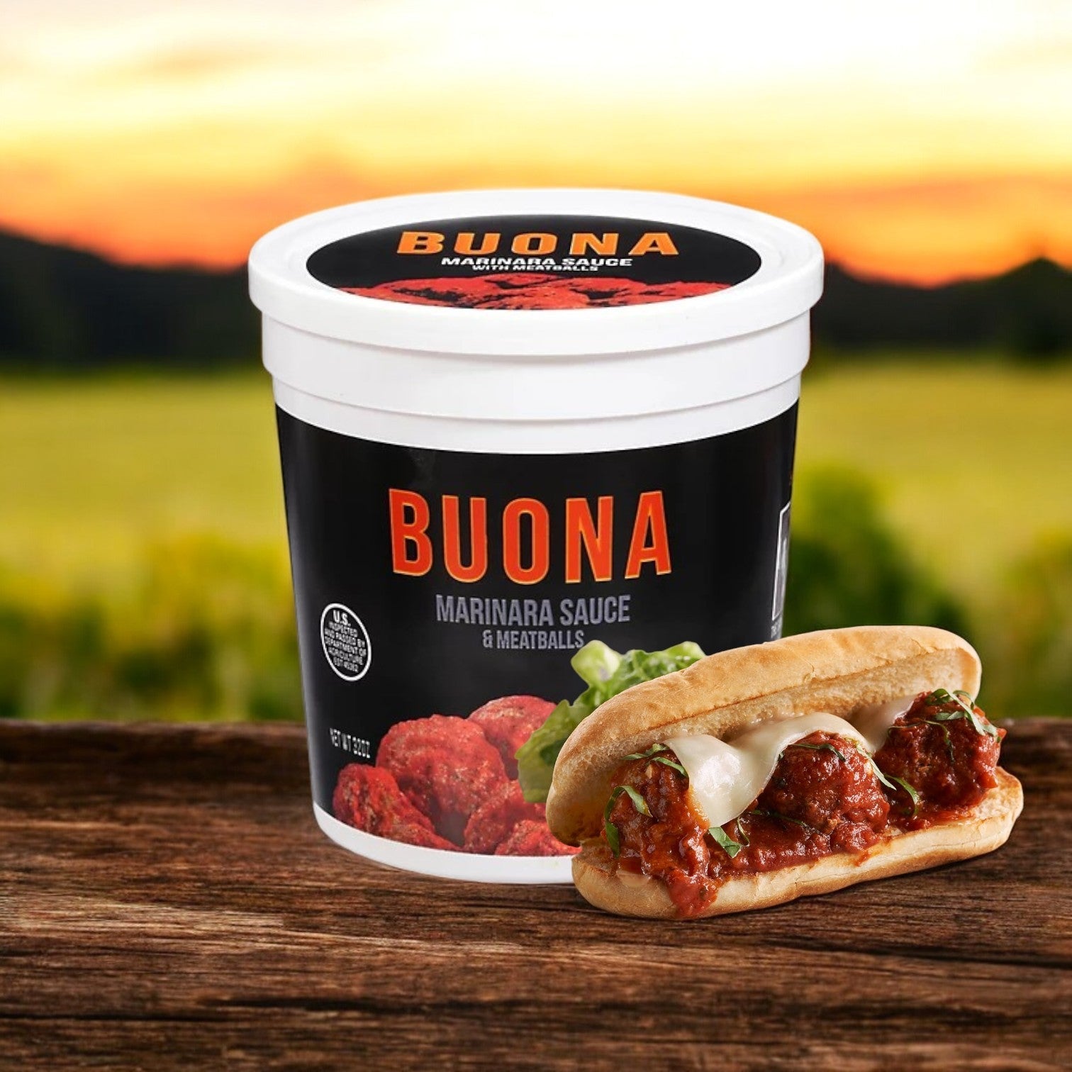 A container of Buona Marinara Sauce & Meatballs – 32 oz is placed beside a hearty meatball sub on a wooden surface, with a blurred outdoor background.