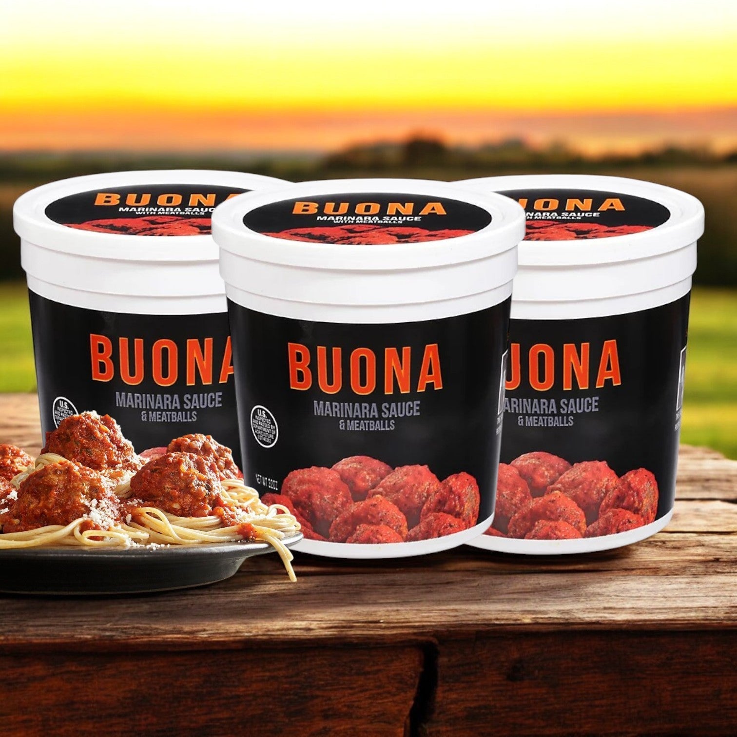 Three packs of Buona Marinara Sauce & Meatballs, each 32 oz., sit on a wooden table with a plate of spaghetti and meatballs exuding an authentic Italian flavor. A sunset landscape graces the background.