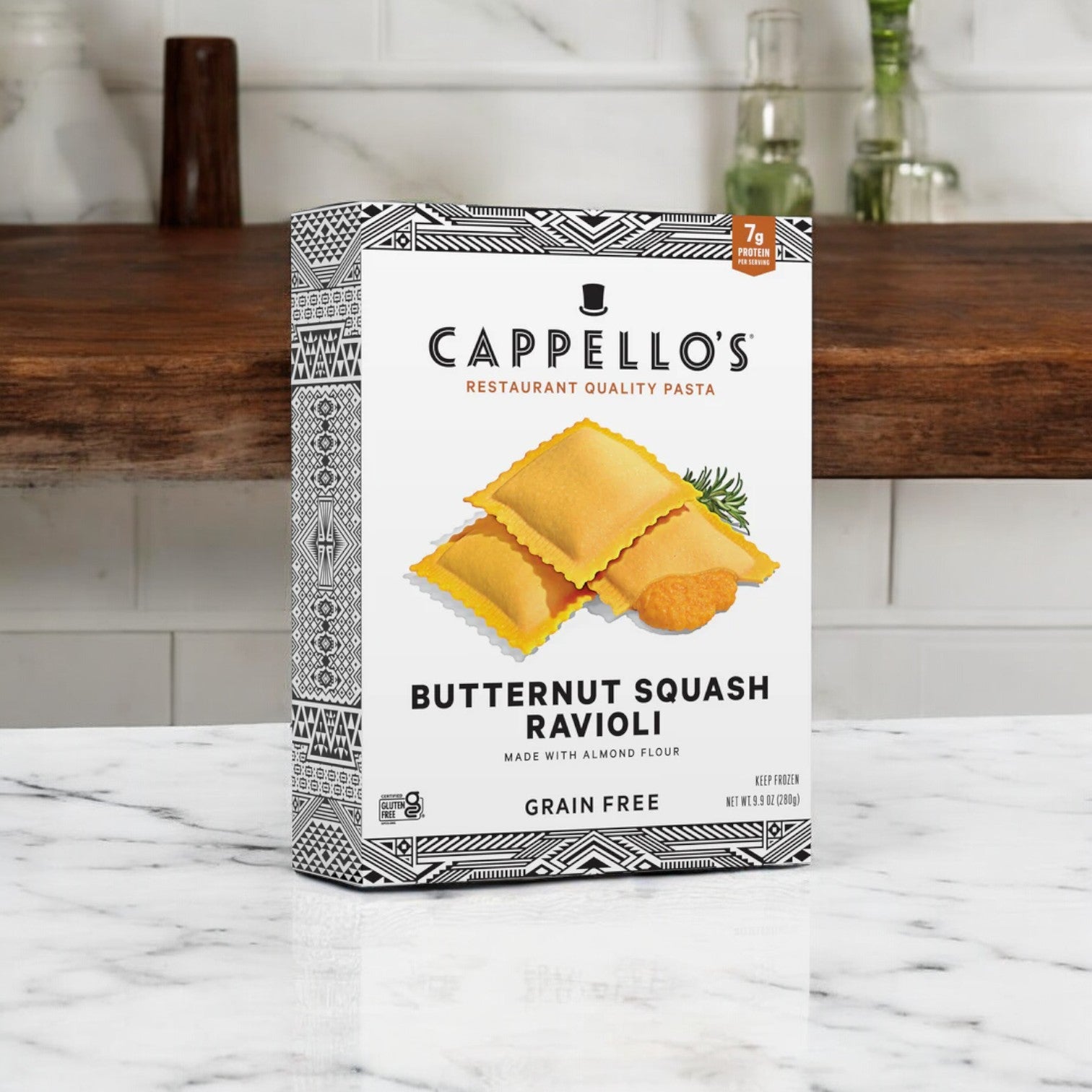 A box of Cappello's Butternut Squash Ravioli, 9.9 oz., sits on a marble countertop against a stylish backsplash. This Italian delight is grain-free and made with almond flour for a unique taste.