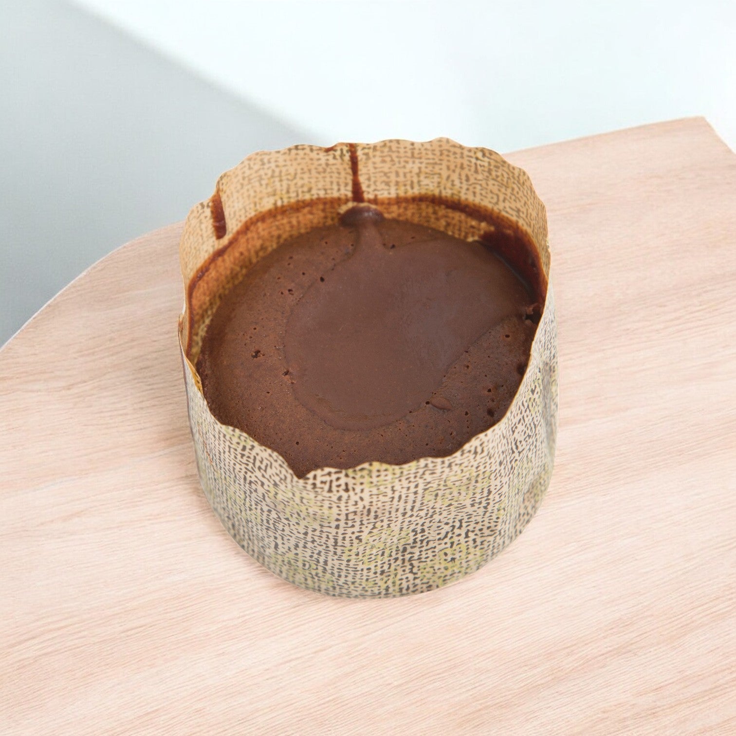 The Sysco Cake Fudge Divine Lava 3", 5 oz., wrapped in brown parchment paper, rests on a wooden surface, offering indulgence from its molten fudge center with every bite.