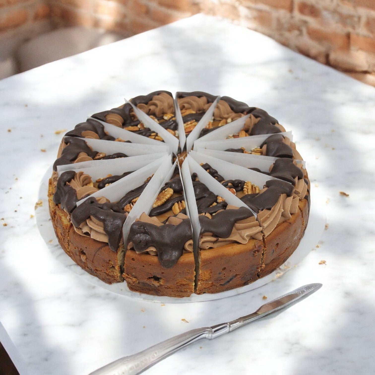 A 12-slice chocolate cake, adorned with chocolate icing, walnuts, and white chocolate decorations, captures the essence of a Chicago dessert. Sitting on a marble surface next to a knife, this delightful treat shares its charm with classic offerings like Eli's Cheesecake Turtle Cheese Cake.