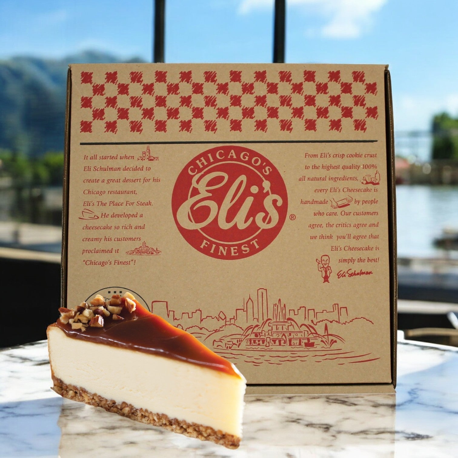 In a sunny outdoor setting, the Elis Cheesecake Caramel Salted Cheesecake from Eli's Cheesecake is presented temptingly beside its "Eli's Chicago's Finest" box. The cake, enriched with caramel and nuts, invites you to savor every delectable slice of this creation.