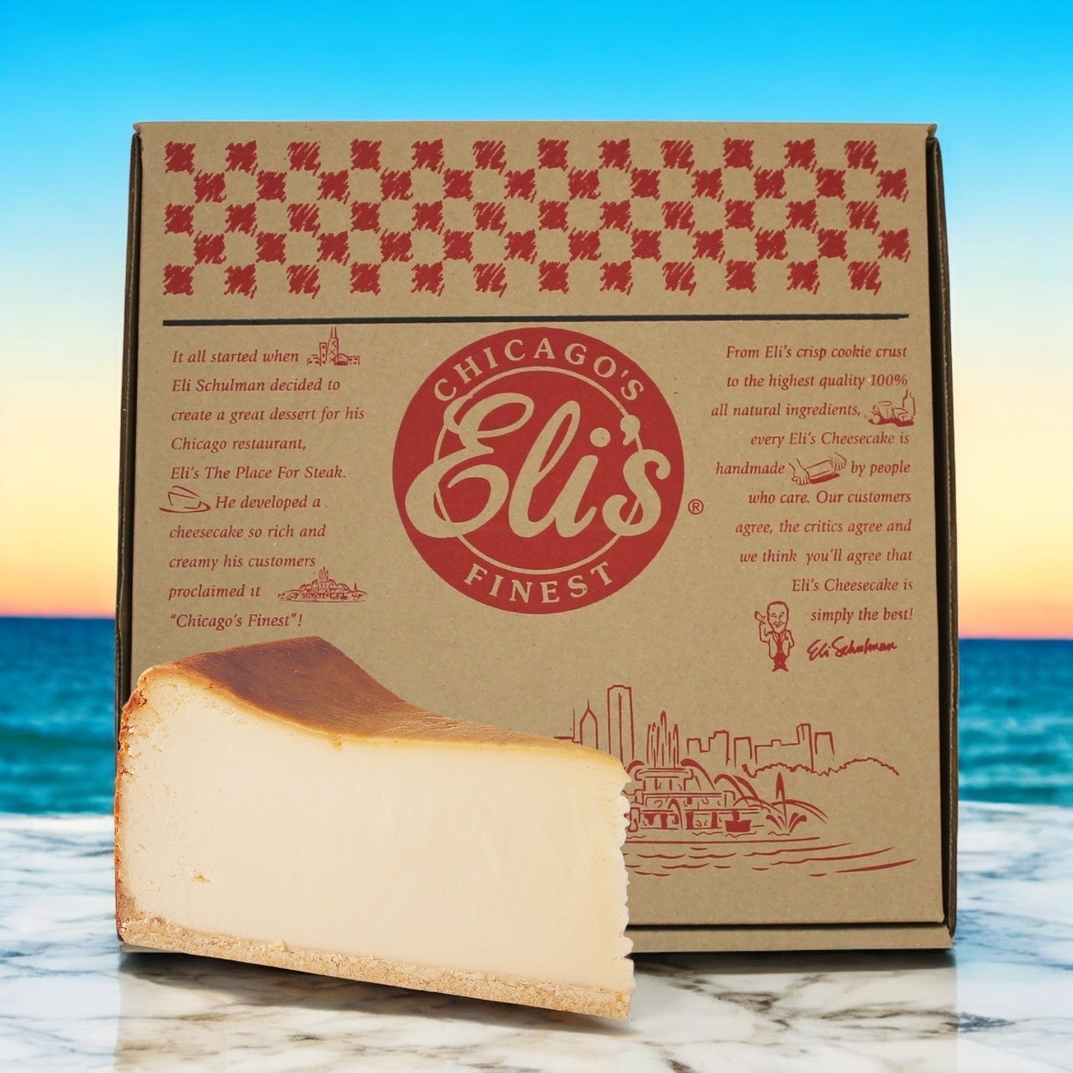 A slice of Eli's Cheesecake, Plain 10" Round, sits before a branded box with text and designs, set against a scenic beach backdrop.
