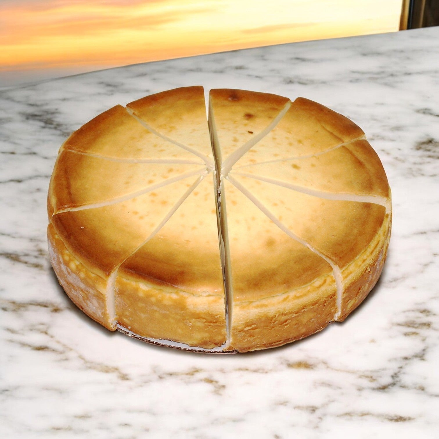 An Eli's Cheesecake, Plain 10" Round Cake from a case of 2, elegantly sliced into 14 pieces, is displayed on a marble surface against a blurred sunset backdrop.