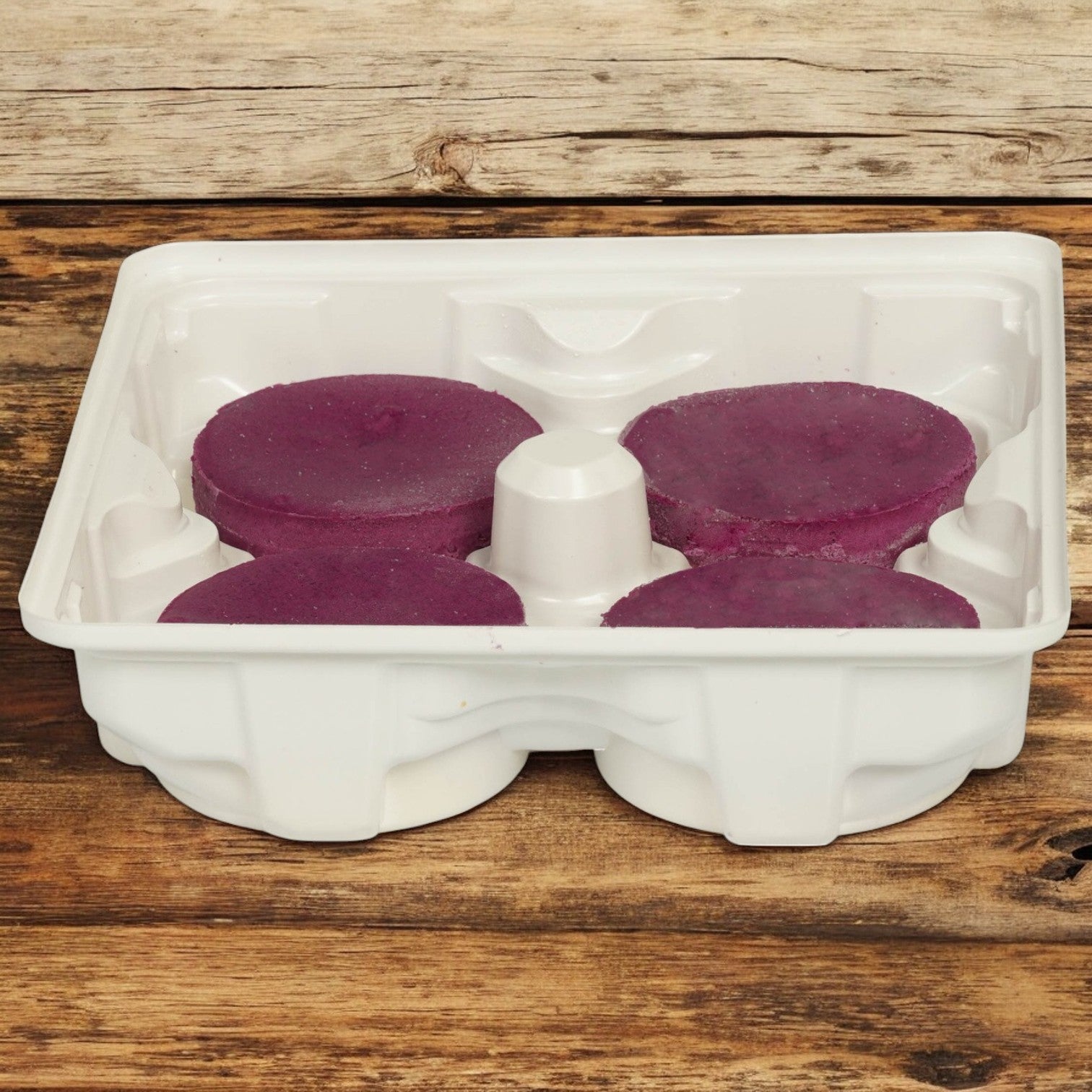 The Sweet Street Cheesecake Ube Individual comes in a plastic container with four round, purple wax melts made from premium ingredients, each in its own compartment on a wooden surface.