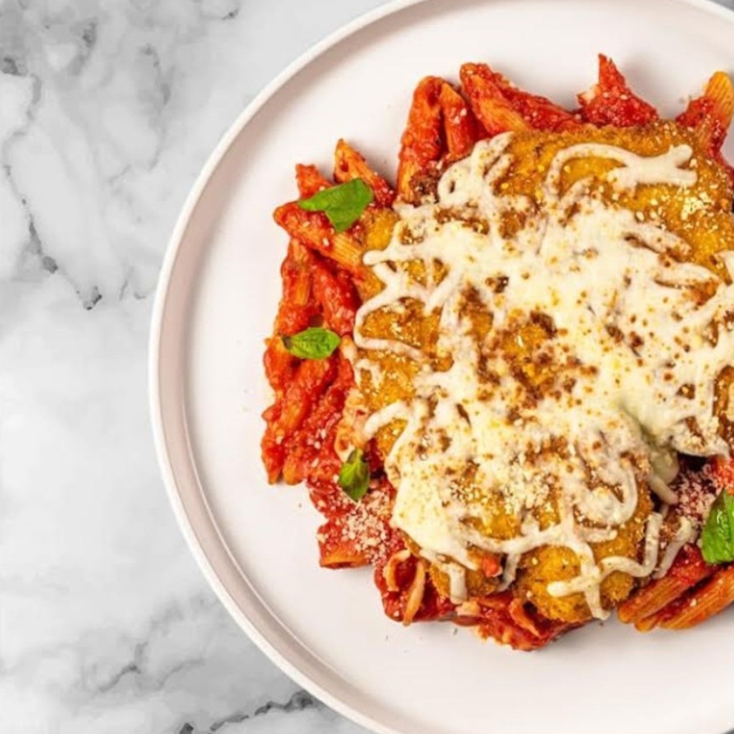 Enjoy an authentic Italian meal with FoodHaul's Chicken Parmesan by Fabio Viviani, featuring penne in red sauce topped with a breaded, cheese-covered chicken patty and garnished with fresh herbs.