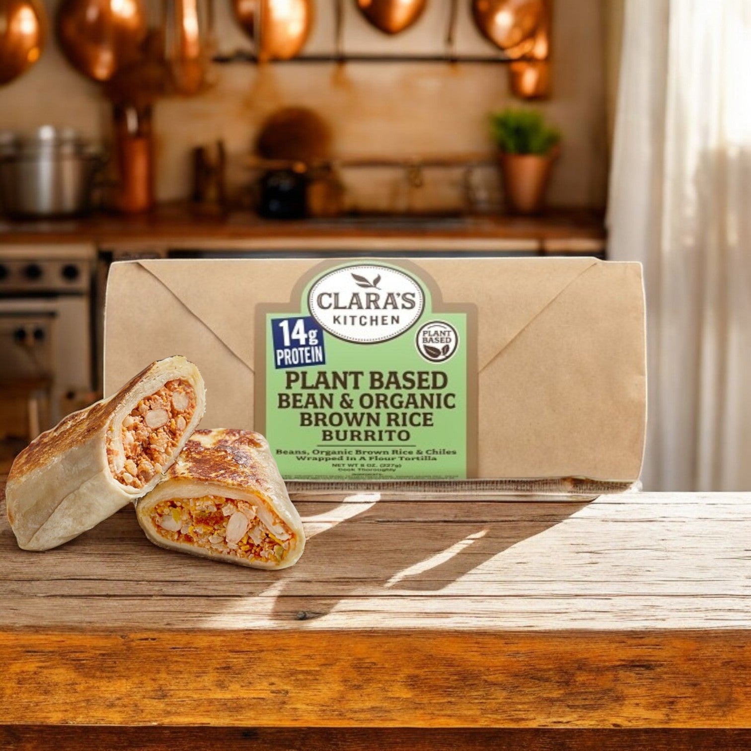 A vegan burrito with plant-based beans, organic brown rice, and plant-based cheese on a wooden kitchen counter features "Clara's Kitchen" packaging with 14g protein. Product: Clara's Kitchen Individually Packaged Vegan Bean & Cheese Burrito, 8 oz.