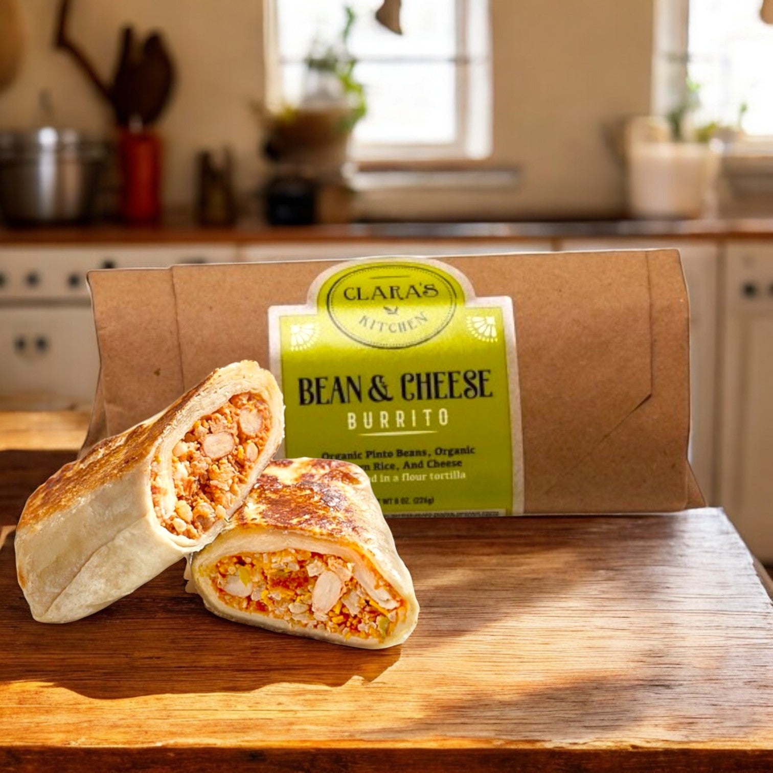 Clara's Kitchen Individually Packaged Bean & Cheese Burrito, 8 oz., is vegetarian-friendly and halved on a wooden surface, showcasing its hearty filling. The wrap can be seen in the background, nestled in a cozy kitchen setting.