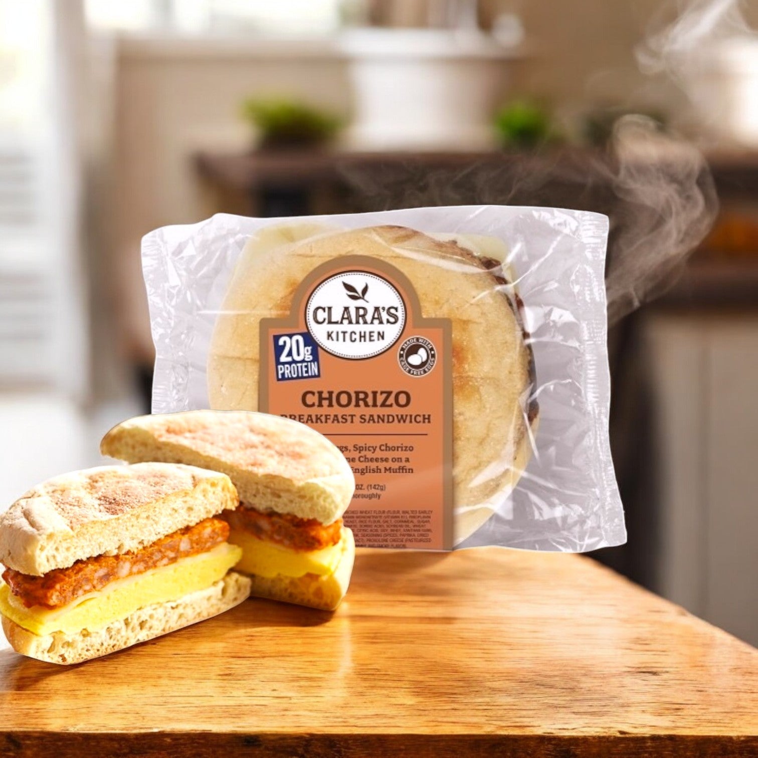 Clara's Kitchen 5oz Individually Packaged Chorizo Breakfast Sandwich, with an English muffin, cheese, egg, and chorizo patty on a wooden surface. Steam rises in the blurred background for a convenient breakfast.