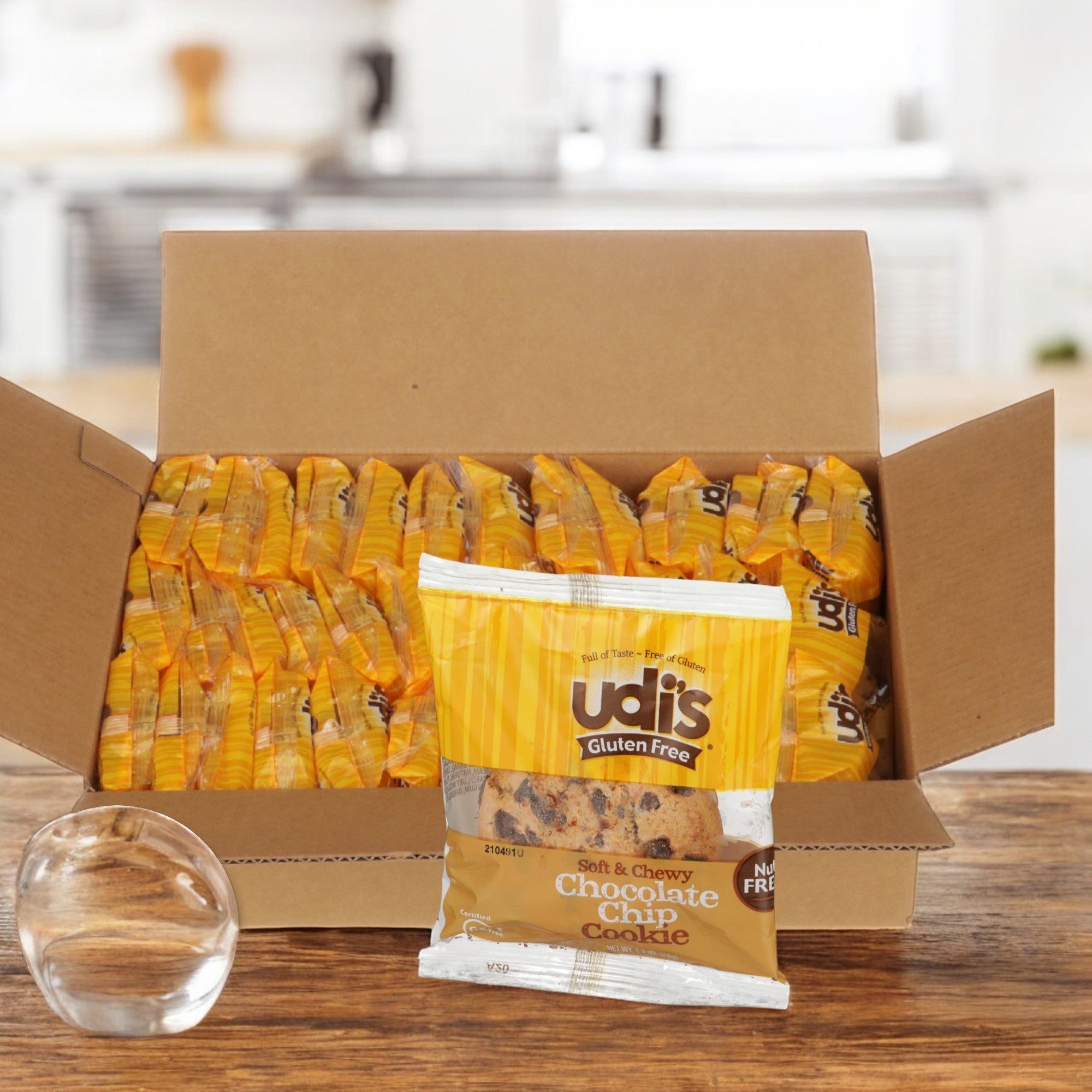 A box from Udi's, Cookie Chocolate Chip Gluten Free - 1 Case, 36 Count is open on the kitchen counter with a semi-sweet chocolate chip cookie package standing invitingly in front.