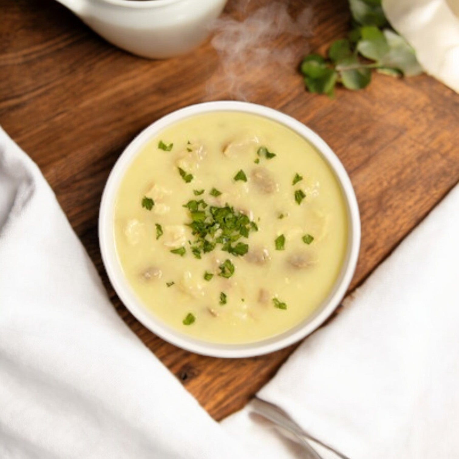 A steaming bowl of Bistro Soups by Vienna Beef, Cream of Chicken with Rice Soup, features premium ingredients and is garnished with herbs on a wooden surface, complemented by a white napkin.
