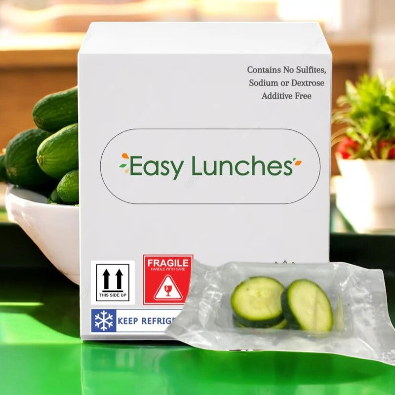 A box labeled "Easy Lunches" sits on a green surface with cucumbers in the background and a plastic packet of Sliced Zucchini, 2.5 oz. - 50 Pack, ready to cook and nutritious with a 7-day shelf life upon delivery.