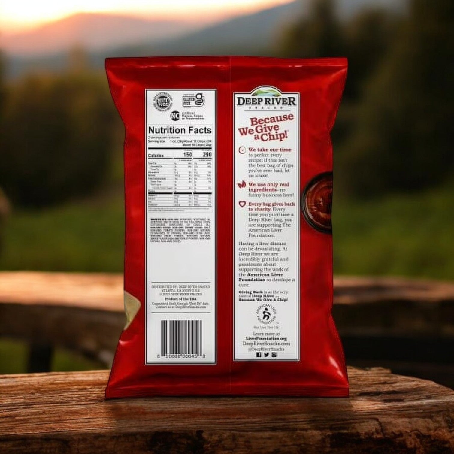 The back of a Deep River Snacks Mesquite BBQ Kettle Potato Chips bag displays its gluten-free and non-GMO status, emphasizing taste and quality. Positioned on a wooden table with an outdoor background, it highlights nutritional info and the brand's commitment to excellence.