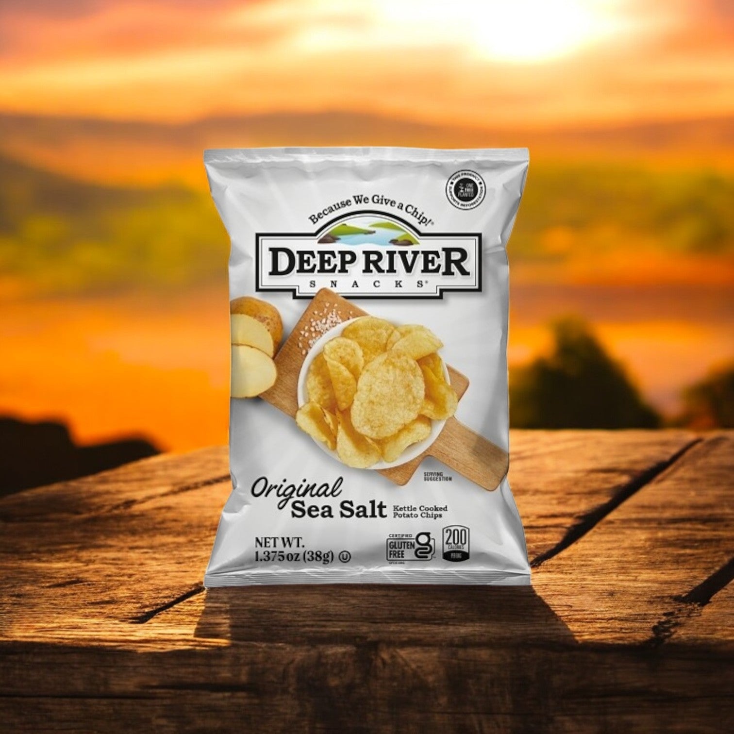 On a wooden table with a sunset backdrop lies a 1.375-ounce bag of Deep River Snacks Original Sea Salt Kettle Potato Chips, which are proudly gluten-free and non-GMO.