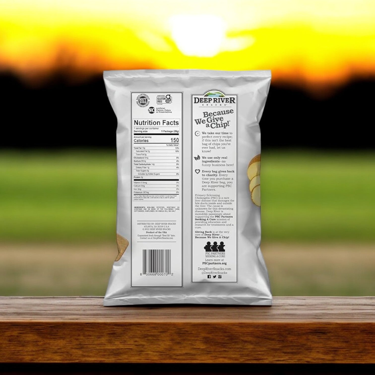 A bag of Deep River Snacks - Original Sea Salt Kettle Potato Chips (2 oz) is placed on a wooden surface, with a blurred sunset creating an ideal evening backdrop.