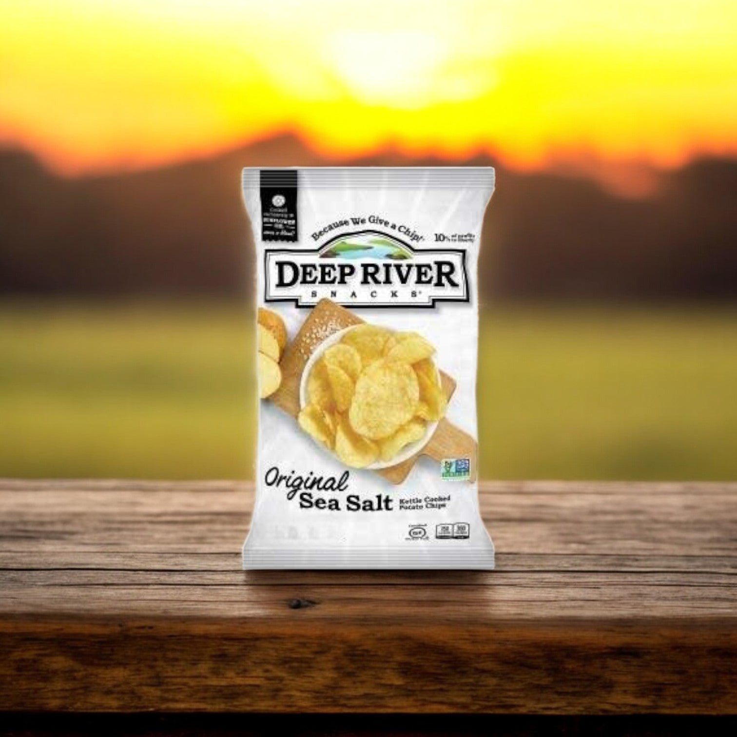 A bag of Deep River Snacks Original Sea Salt Kettle Potato Chips, 1 Ounce, 80 per case, is placed on a wooden surface with a blurred sunset in the background.