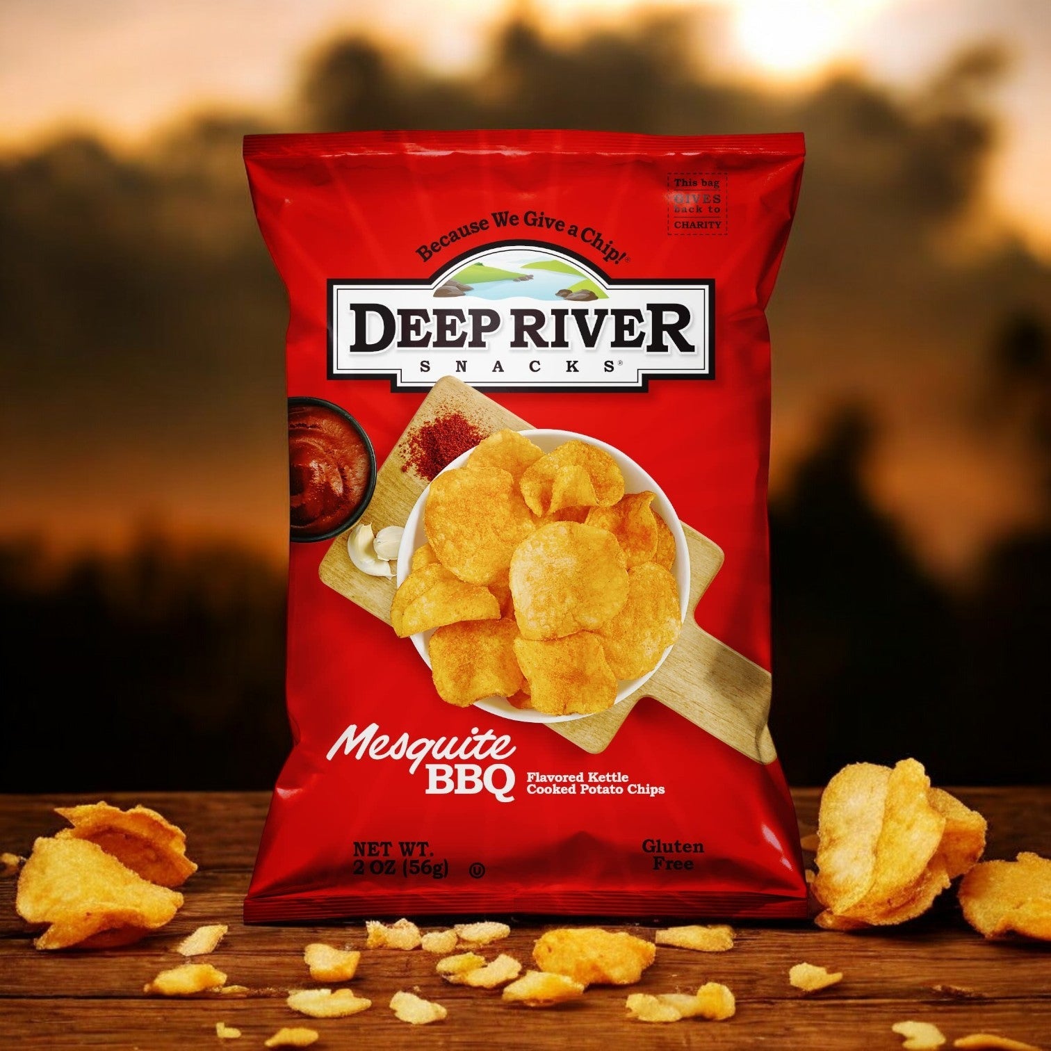 A 2-ounce bag of Deep River Snacks Mesquite BBQ Kettle Potato Chips, featuring a Non-GMO label, with scattered chips and a sunset backdrop.