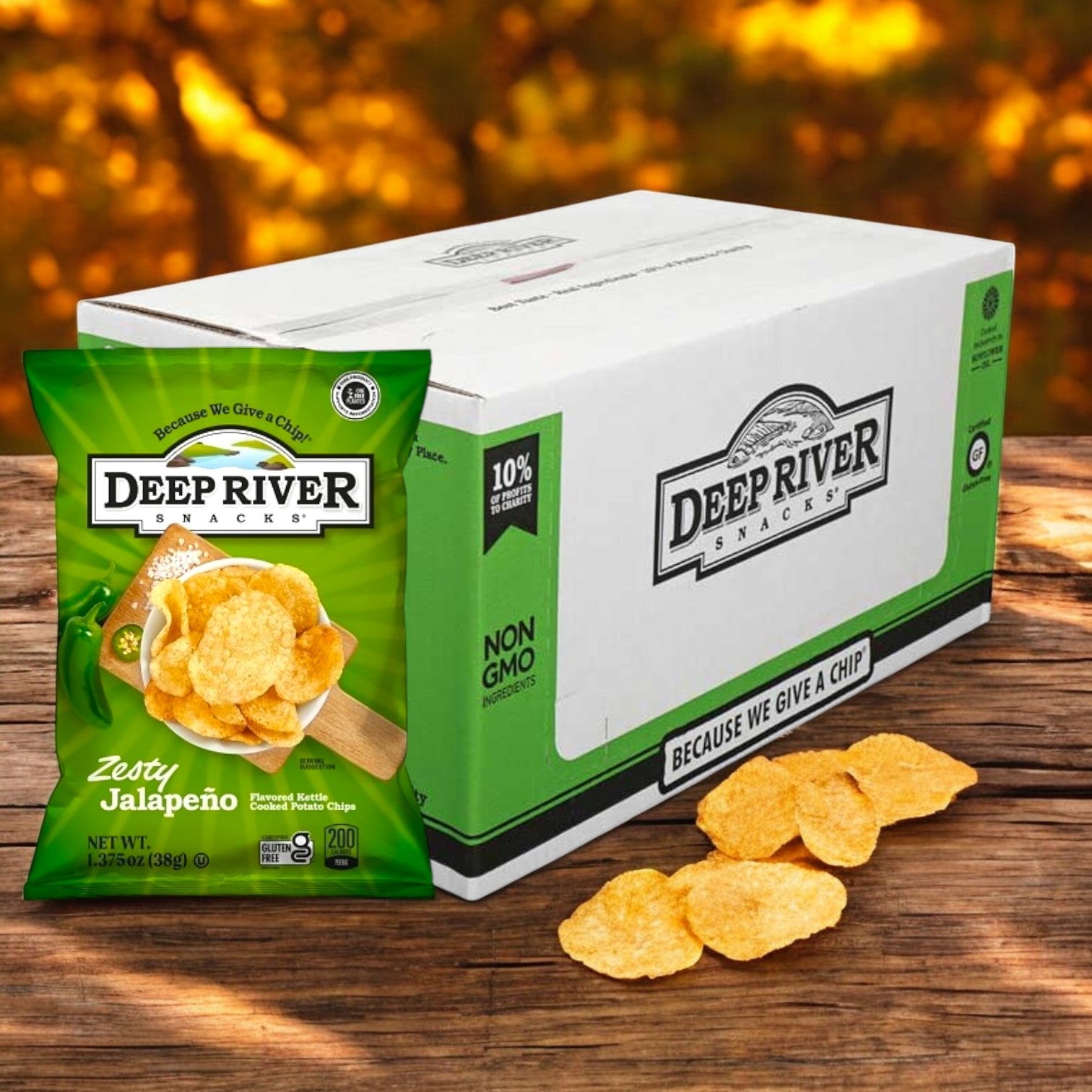 Deep River Snacks Zesty Jalapeno Kettle Potato Chips, 1.375 oz, tumble from the bag onto wood with a branded box softly blurred in an outdoor backdrop.