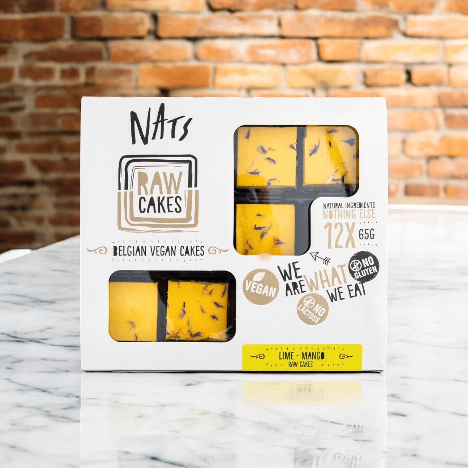 A box of Nats Vegan Cakes includes 12 lime mango dessert cakes, each 2.29 oz. The packaging features a cut-out window to showcase these Belgian plant-based treats made with natural ingredients for a delightful lime mango experience.