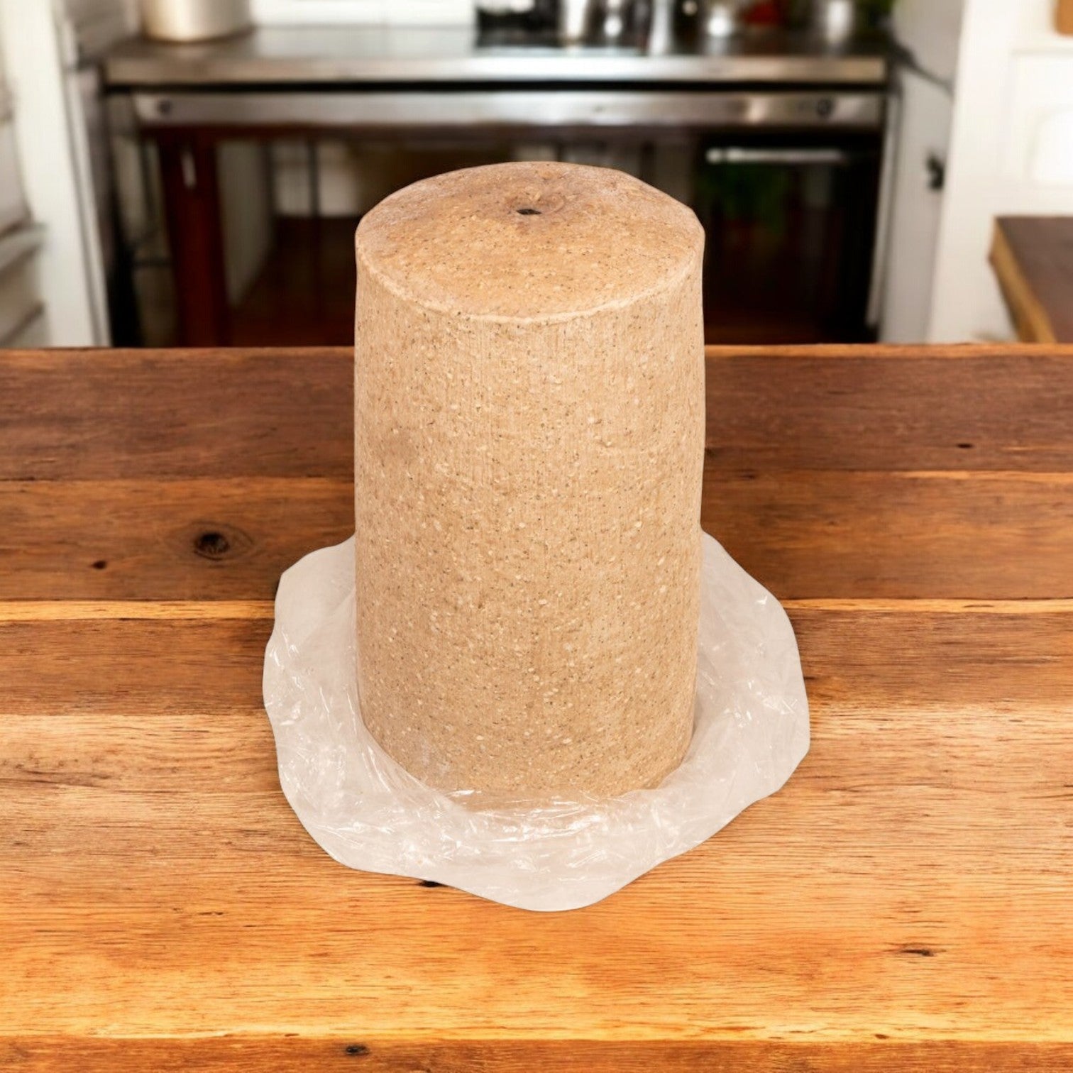 A 20 lb Devanco Foods Frozen Halal Gyro Cone, seasoned with Mediterranean spices, rests on a wooden table with clear plastic at its base. Kitchen equipment is visible in the background.