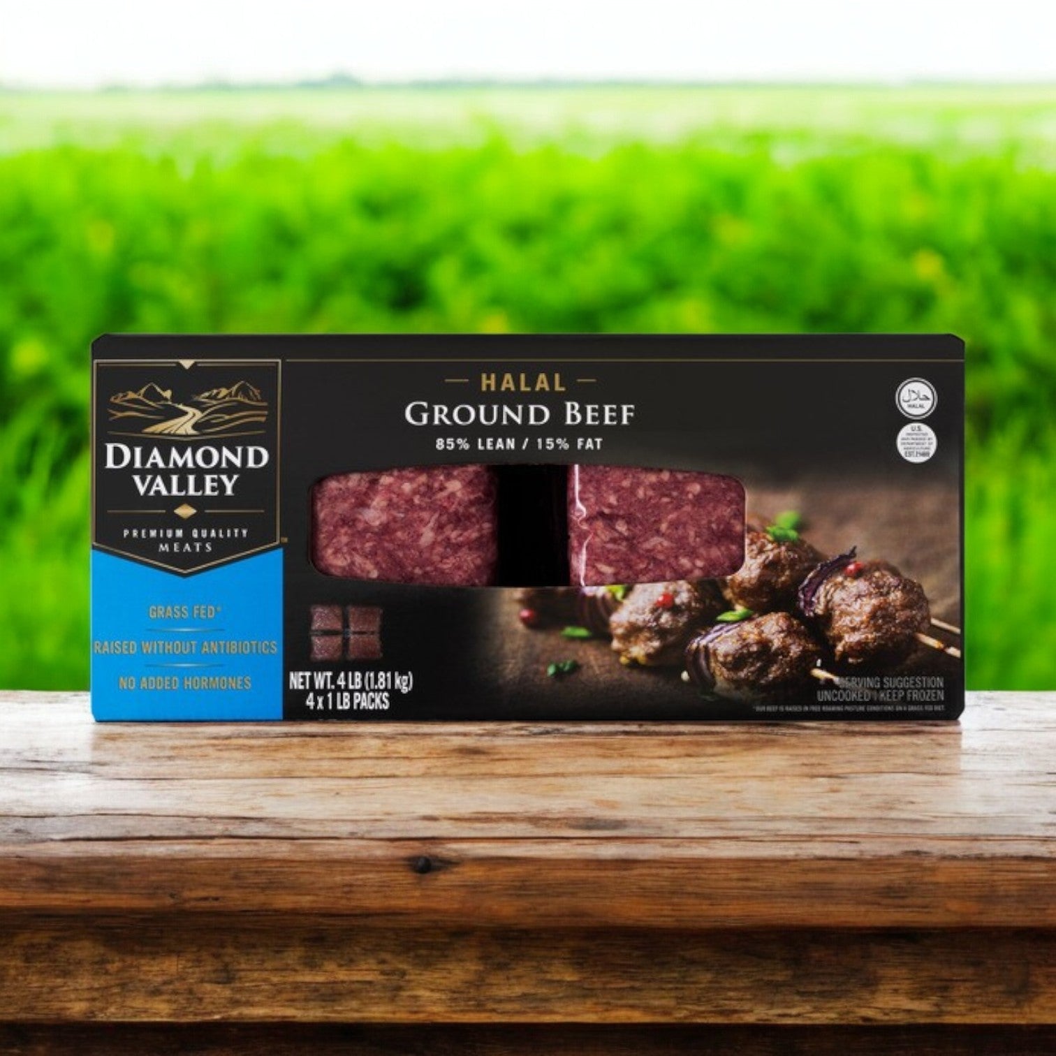 A package of New Zealand Spring Lamb's Diamond Valley Halal Ground Beef, 85% lean and 15% fat, rests on a wooden surface against a grassy field. Grass-fed and hormone-free, it offers quality similar to premium seafood or yellowfin tuna steaks.
