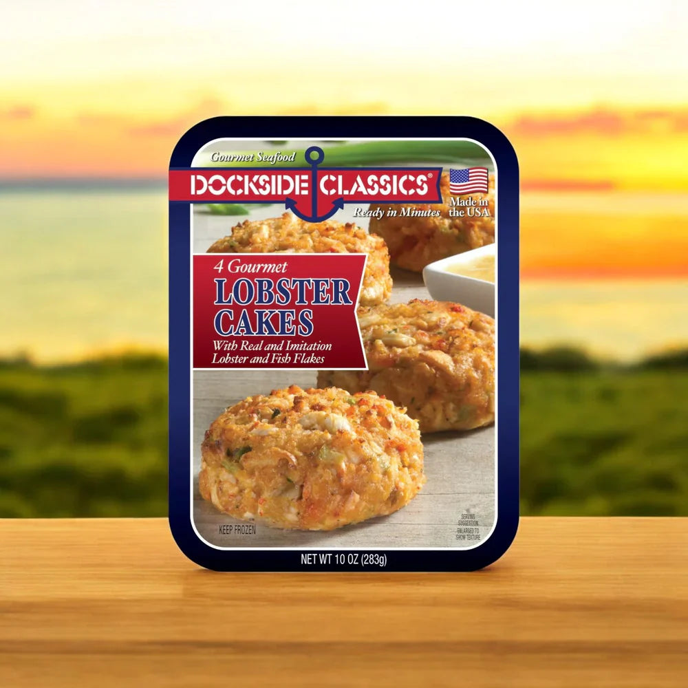 A package of Dockside Classics Gourmet Crab Cakes and Combo rests on a wooden table, with a sunset over the water in the background, offering a premium seafood experience.