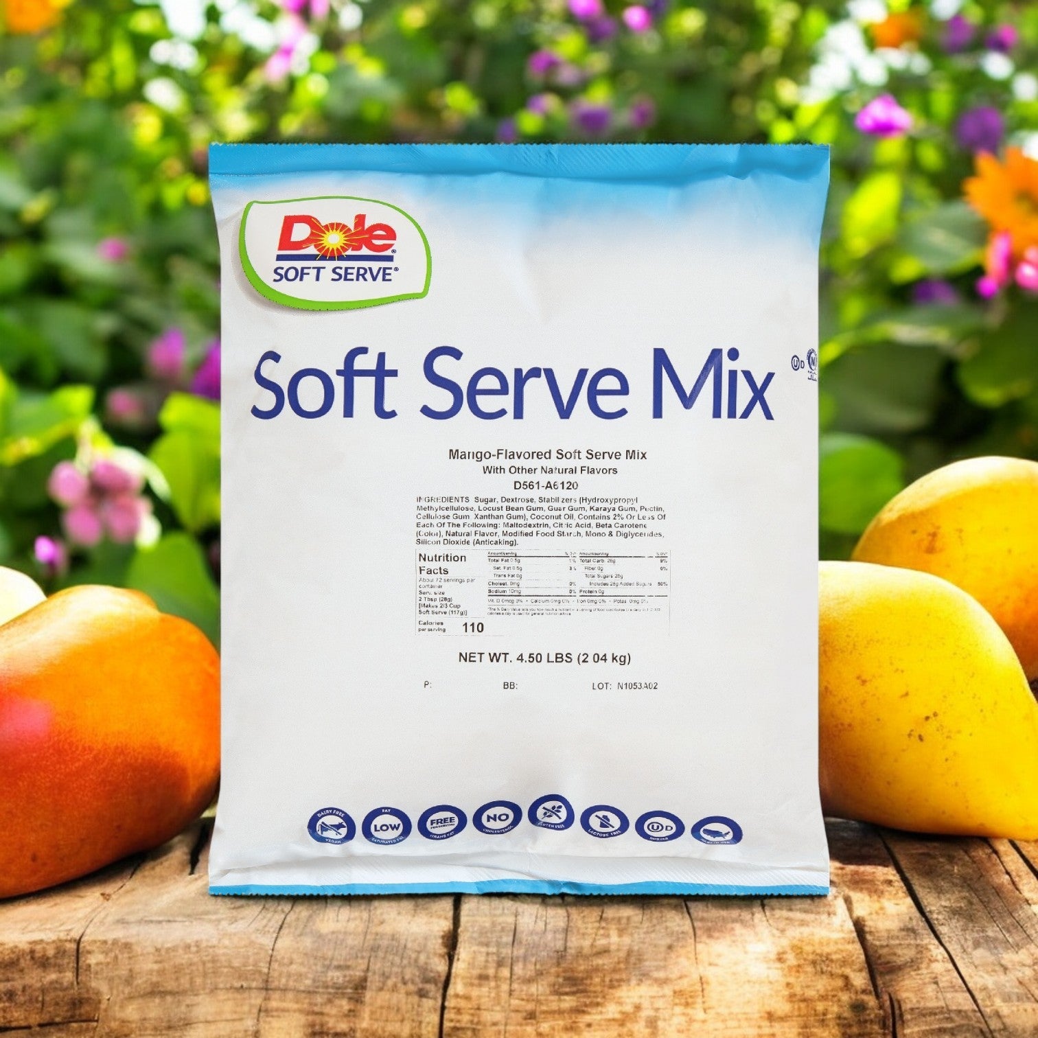 A pack of Dole Soft Serve Mix Mango, featuring four 4.5 lb. bags and brimming with tropical flavor, rests on a wooden surface surrounded by fresh mangoes with blurred foliage in the background.
