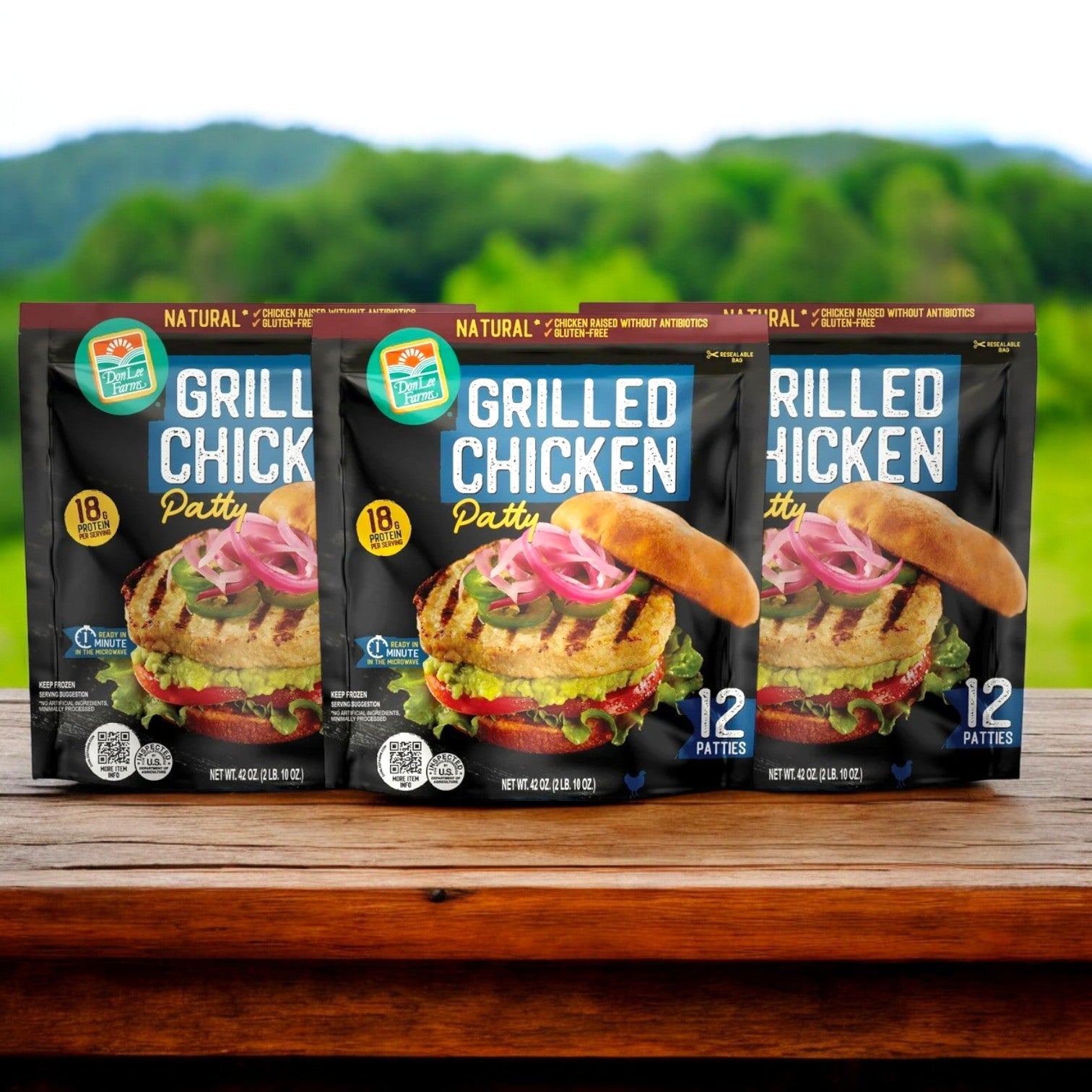 Three packages of Don Lee Farms Chicken Patties, featuring 36 delicious and fully cooked all-natural patties, are displayed on a wooden table against a scenic outdoor backdrop.