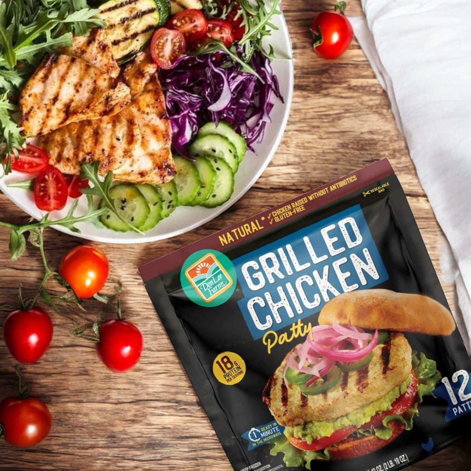 A grilled chicken salad with greens and vegetables is enticingly displayed beside a package of Don Lee Farms Chicken Patties, 36-Count – Delicious, All-Natural & Fully Cooked, on a wooden surface, showcasing the high-quality ingredients.