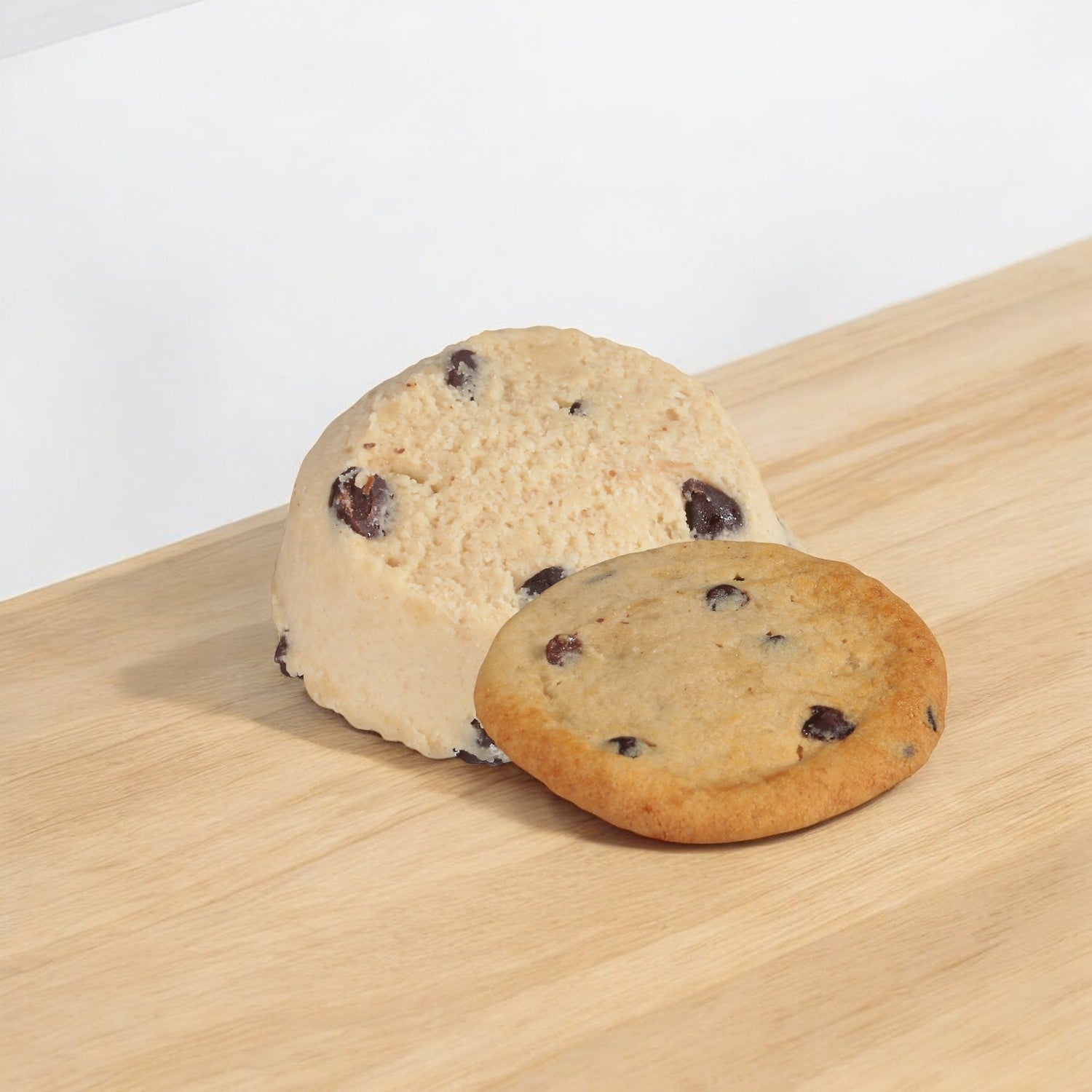 A dome-shaped ice cream paired with a chocolate chip cookie, showcasing pieces of Otis Spunkmeyer Dough Cookie Chocolate Chip with embedded chocolate chips, sits enticingly on a wooden surface.