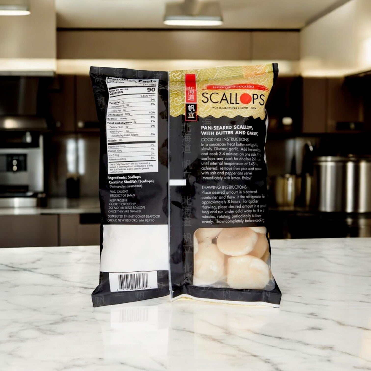 Two bags of Kirkland Signature East Coast Seafood Japanese Hokkaido Scallops, Raw, 18-23 ct, 2 lbs are shown on a marble countertop in a modern kitchen, displaying both front and back packaging with product details.
