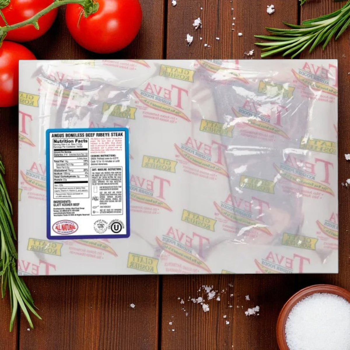 Teva Kosher Foods Teva Glatt Kosher Angus Boneless Ribeye Steak – 2-Count Pack (3 Total Packs) in vacuum-sealed packaging is displayed on a wooden table with tomatoes, rosemary, and a bowl of coarse salt.