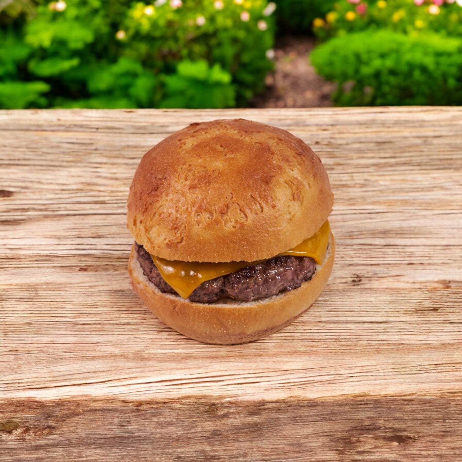 An Udi's gluten-free hamburger bun, individually wrapped (4 in., 24 pack case), holds a beef patty and cheese slice, placed on a wooden surface with greenery. Its soft and sturdy texture ensures each bite is delightful and satisfying.