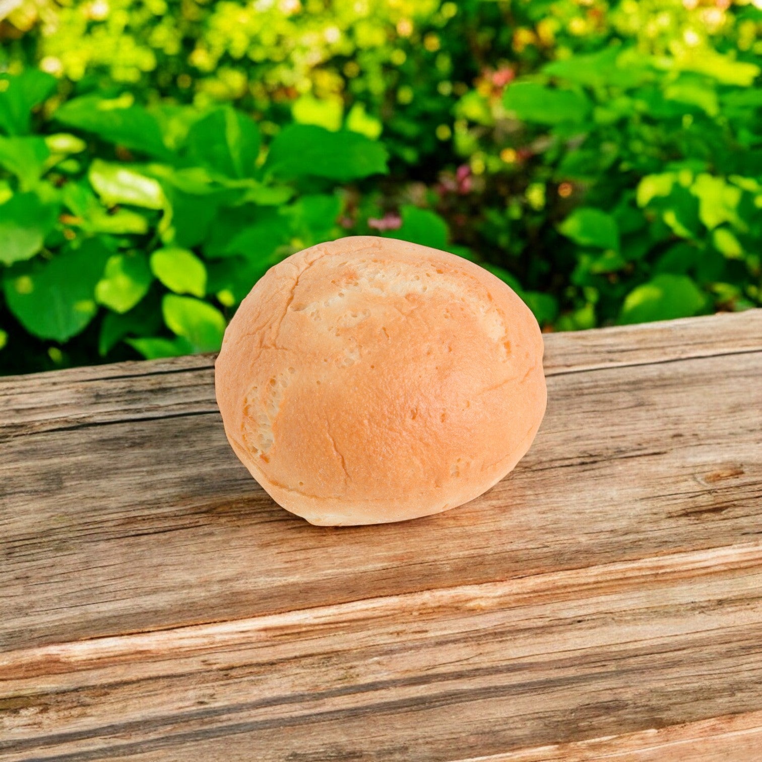 An Udi's gluten-free hamburger bun, individually wrapped and soft yet sturdy, sits on a wooden surface, with vibrant green foliage in the backdrop.