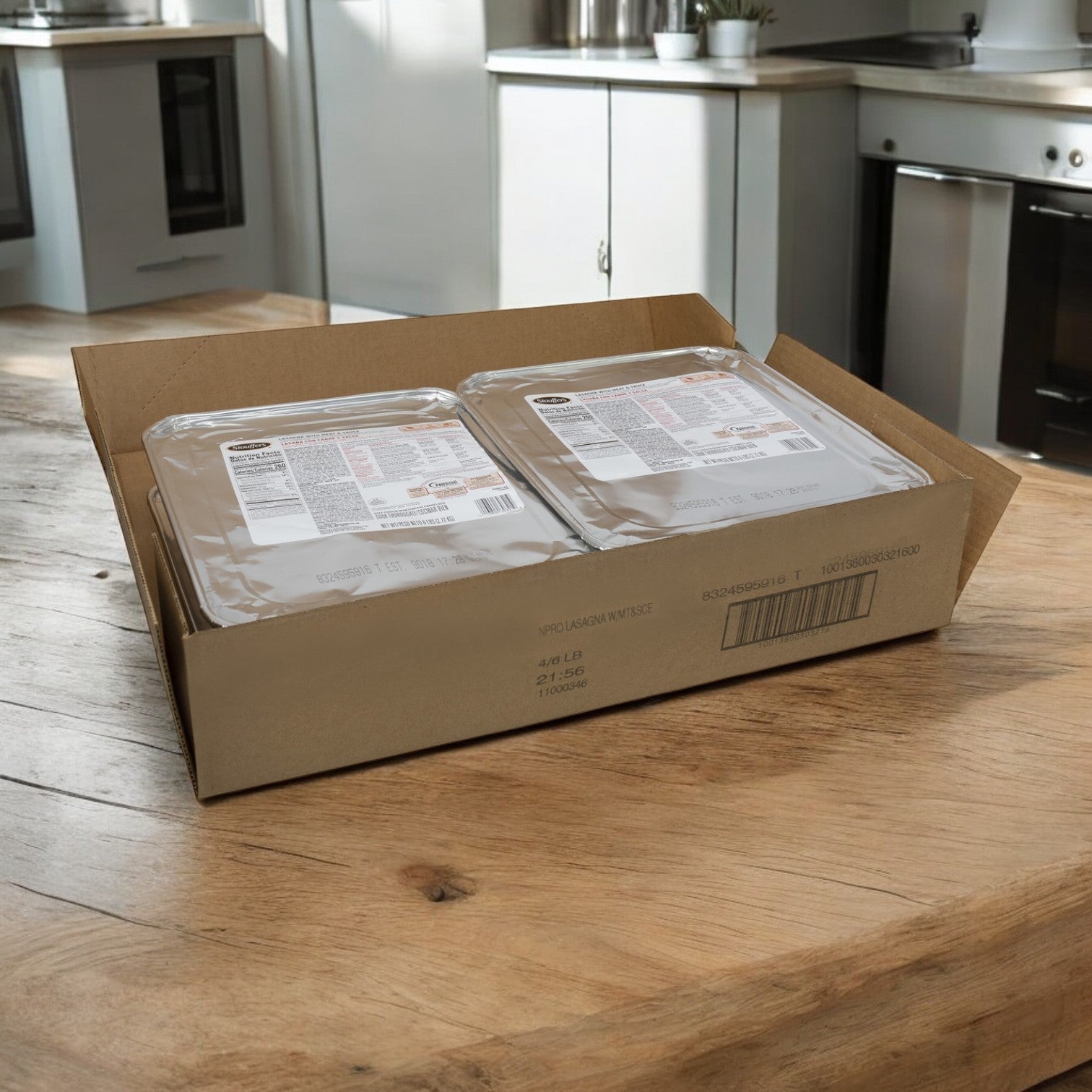 Two sealed foil trays of Stouffer's Entree Lasagna Meat sit in an open case on a wooden kitchen table, with blurred appliances and countertop softly fading into the background—a truly convenient meal solution.