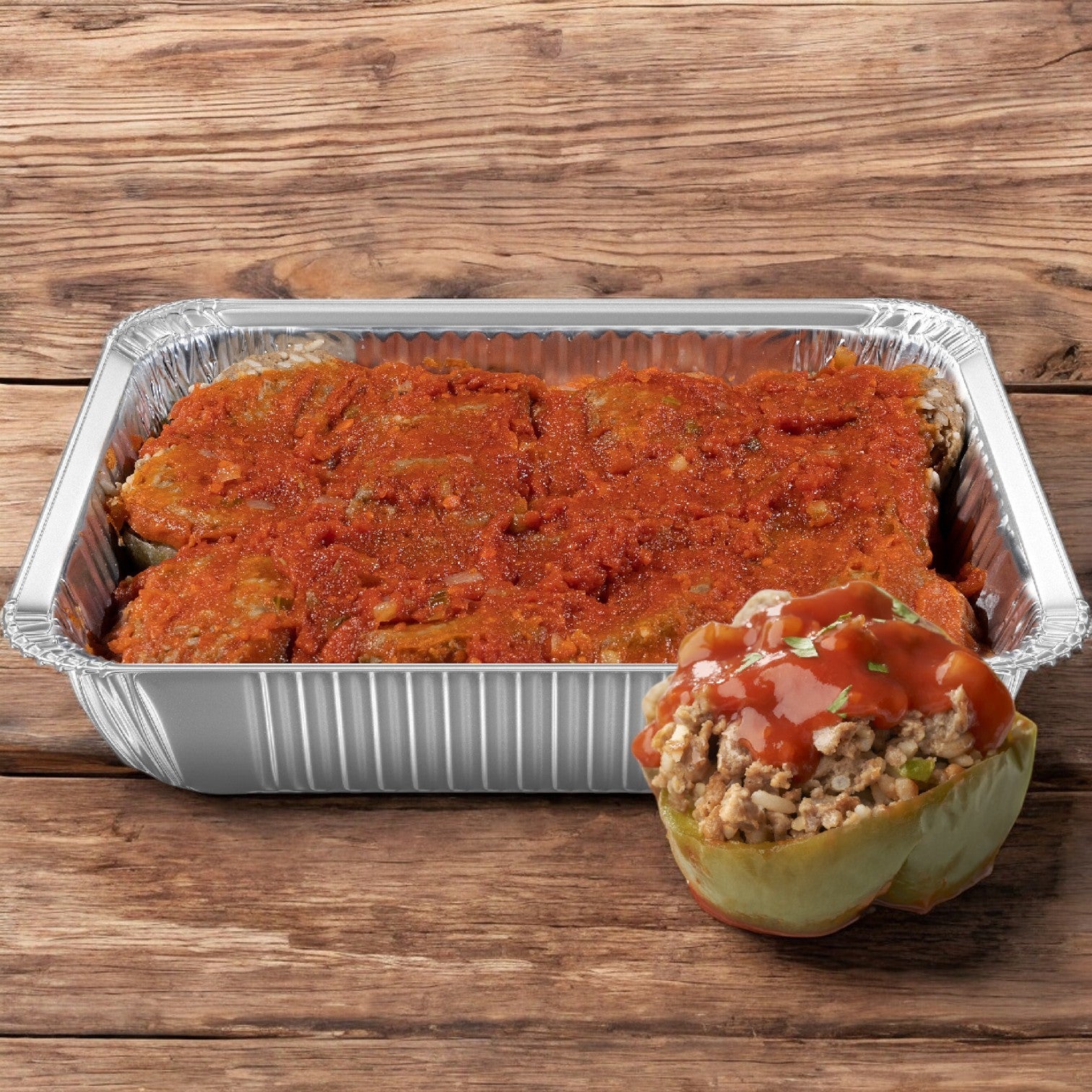 A Sysco Classic Entree tray of green peppers stuffed and topped with red sauce is displayed next to a single pepper on a wooden surface, highlighting the flavorful filling.