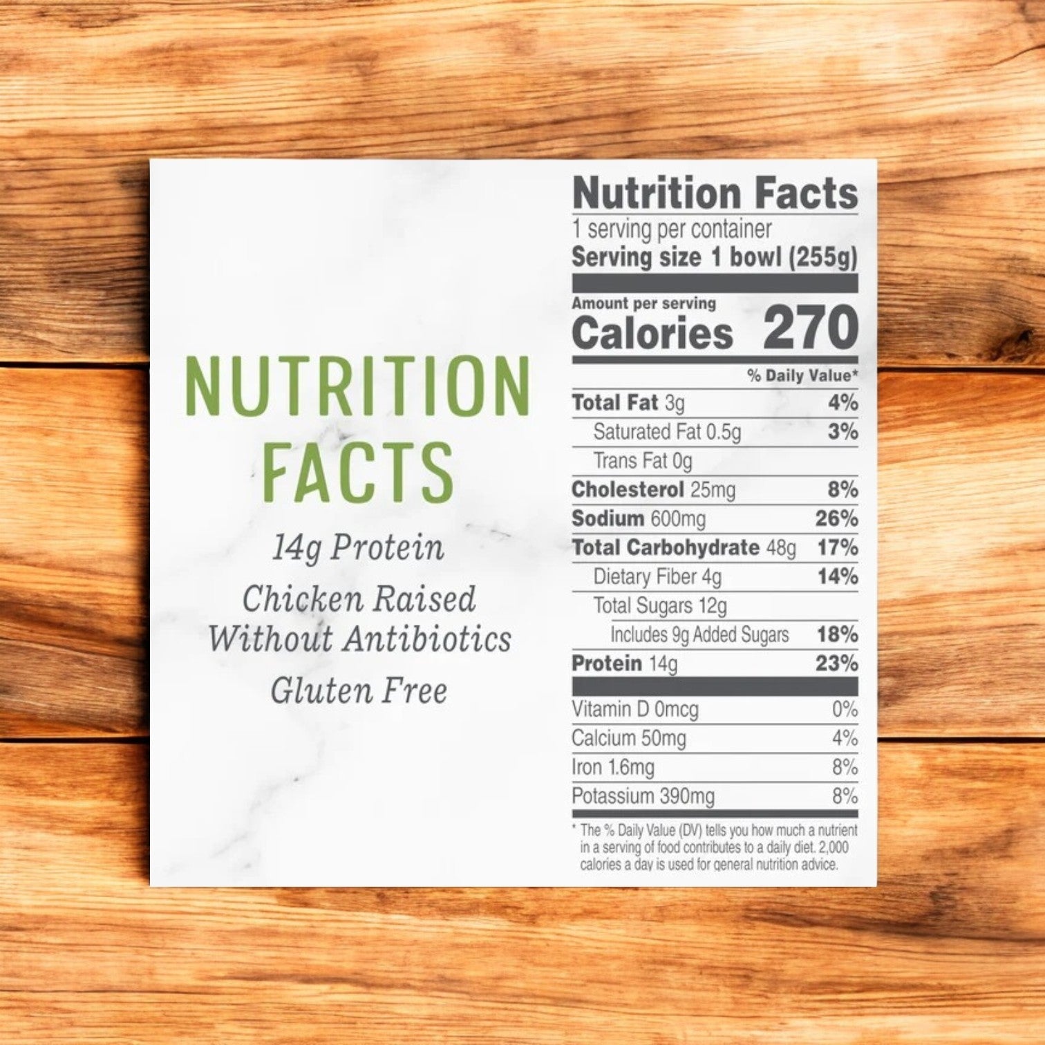 The nutrition facts label for Evol Teriyaki Chicken Frozen Meal, 9 oz details that each 255g serving contains 270 calories, with comprehensive information on fat, cholesterol, sodium, carbs, protein content, and allergy data prominently displayed on a wooden surface.