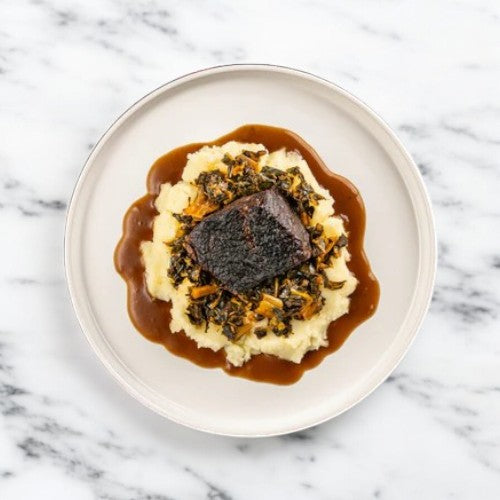 Enjoy the Easy Lunches FoodHaul Braised Short Ribs, accompanied by creamy mashed potatoes, fresh greens, and shredded carrots drizzled with a rich sauce. Presented on a white plate for a premium ready-to-cook at-home experience.