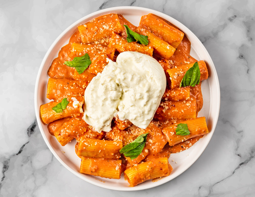 A serving of FoodHaul Spicy Rigatoni garnished with creamy tomato sauce, ricotta cheese, and fresh basil leaves.