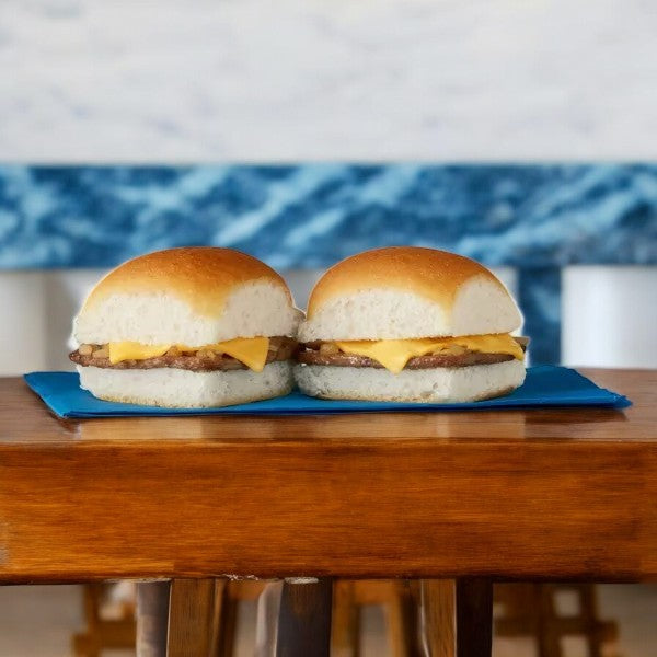 Two White Castle Microwaveable Frozen Cheeseburger Sliders with beef patties and cheese are set on a wooden table against a blurred blue and white backdrop.