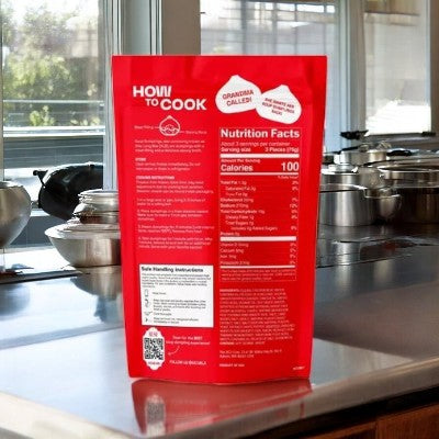 A MiLa Frozen Soup Dumpling - Chicken sits elegantly on a stainless steel kitchen counter amid pots and pans, promising tender meat wrapped in delicate dough.